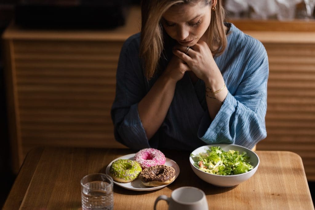a woman struggling between eating a salad or donuts, showing how important medical billing for eating disorder treatment centers is